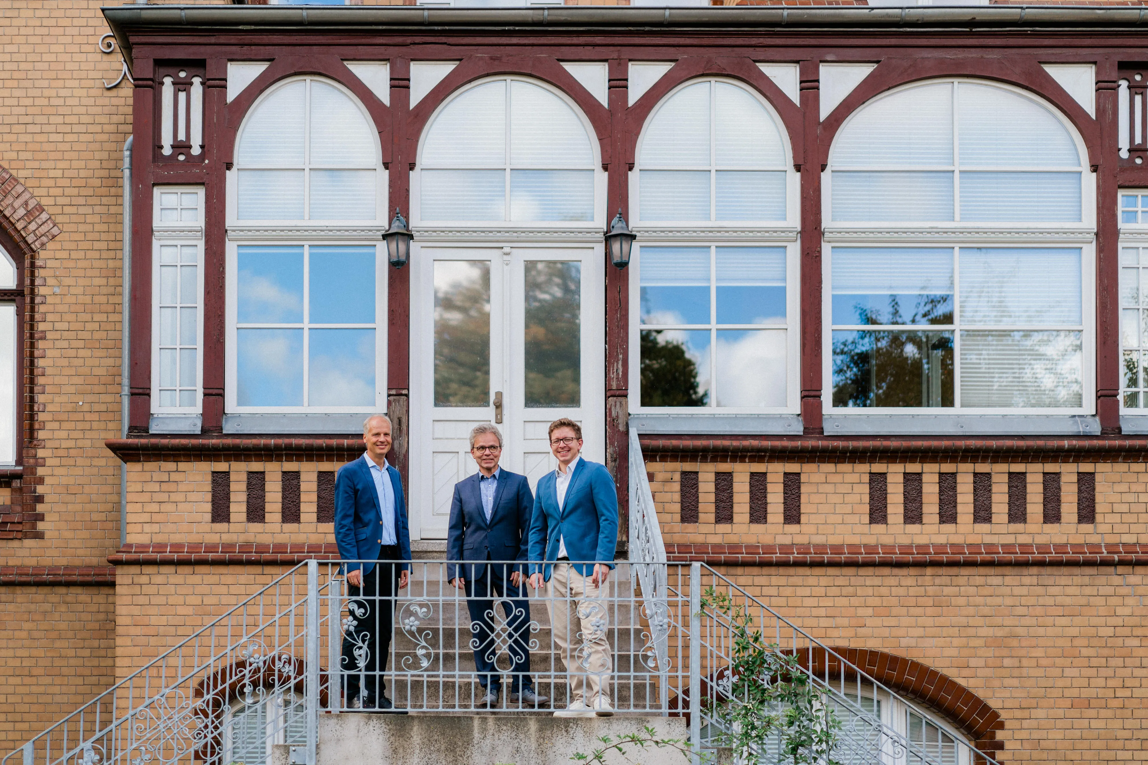 Der Eingangsbereich eines historischen Gebäudes, in dem sich ein Büro von FRP.tax befindet, davor stehen zwei Mitglieder der Geschäftsführung.