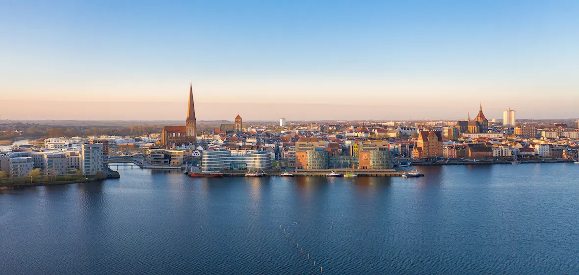 Panoramaansicht von Rostock mit dem historischen Stadthafen, der Marienkirche und modernen Gebäuden entlang der Warnow, die die Verbindung von Tradition und Fortschritt bei FRP.tax symbolisiert.